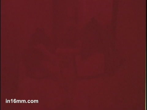 The still from the 'Puffs Tissues' commercial is predominantly a red-hued image, creating a warm and inviting atmosphere. The composition is blurry, obscuring specific details, likely focusing on conveying emotion or ambiance rather than clear visuals. It seems to capture a moment of intimacy or comfort, aligning with the branding of Puffs as a soothing, gentle tissue option.