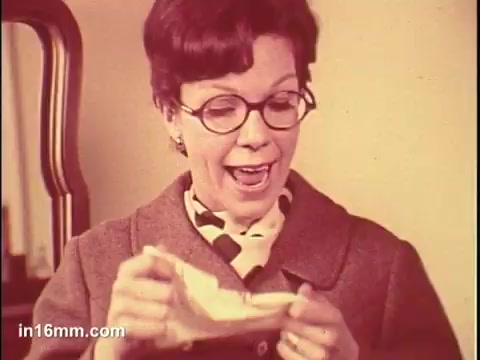 The still features a woman with glasses joyfully holding a tissue from a box labeled 'Puffs.' Her expression conveys satisfaction, suggesting a positive experience with the product. The background appears simple, focusing attention on her and the tissue, highlighting the commercial's promotional message.