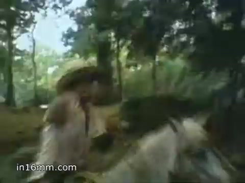 The still from the 1980 Peace Corps Public Service Announcement captures a moment in a lush, green environment. It features an individual in a hat riding a horse, likely portraying the adventurous and challenging nature of Peace Corps work. The visual emphasizes themes of dedication and service, aligning with the tagline 'The toughest job you'll ever love.' The overall tone is one of optimism and commitment to community engagement.