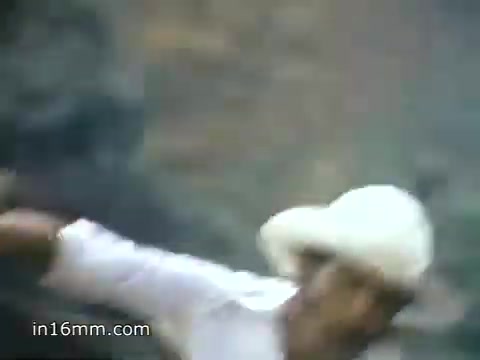 The still from the 1980 Peace Corps Public Service Announcement features a person in a white hat, engaged in an outdoor activity, possibly demonstrating service or community engagement. The background appears to be natural scenery, emphasizing the rugged and meaningful nature of the Peace Corps experience. The phrase 'The toughest job you'll ever love' encapsulates the message of commitment and passion for service.