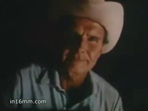 The still from the 1980 Peace Corps Public Service Announcement features a person, likely a volunteer, wearing a wide-brimmed cowboy hat. The lighting creates a dramatic contrast, highlighting the character’s face and expression. The hawk's approach evokes a sense of determination and commitment, emphasizing the slogan, 'The toughest job you'll ever love,' which frames the Peace Corps experience as challenging yet rewarding. The vintage 16mm aesthetic adds a nostalgic touch to the visual.
