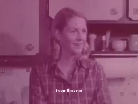 The still features a woman with a smile, likely in a kitchen setting, indicative of the 1970s. She wears a plaid shirt, suggesting a casual, domestic environment. The colors are muted, characteristic of 16mm film aesthetics, and the background includes kitchen items, hinting at the film's focus on domestic cooking or lifestyle themes associated with Imperial Margarine. The overall tone is warm and nostalgic, typical of advertisements from that era.