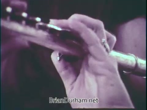 The still shows a close-up of a hand playing a flute, emphasizing the delicate finger positioning on the instrument. This imagery aligns with the theme of supporting music education in schools, highlighting the importance of music and instrument performance.