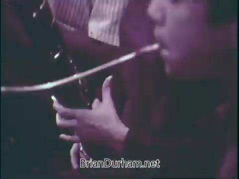 The still features a close-up of a young musician playing a woodwind instrument, possibly a clarinet. The focus is on their hands and the instrument, with a blurred background suggesting other musicians or an audience. The overall tone emphasizes engagement with music, highlighting the importance of supporting music education in schools.