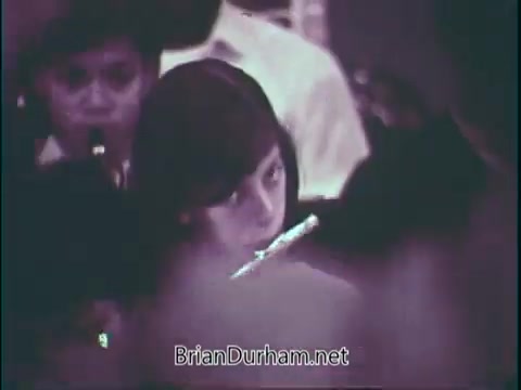 The still from 'Support Music In Your School - PSA' features a young girl playing a flute in a group setting. She appears focused and engaged in her music, with blurred figures around her suggesting a supportive environment of fellow musicians. The overall tone emphasizes the importance of music education within schools.