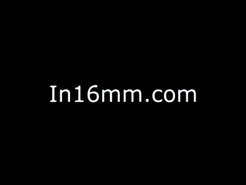 The still features a plain black background with the text 'In16mm.com' prominently displayed in white font. This image serves as a simple title or branding element associated with the film format or project, likely indicating where to find more information or content related to 16mm film. In the context of the PSA, it may function as a transition or ending screen.