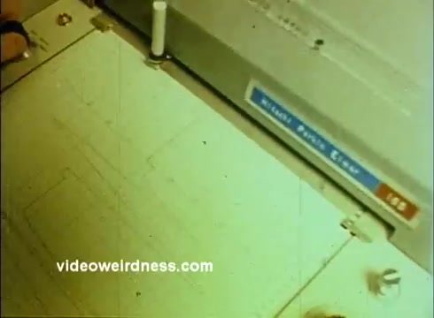 The still from the 'Sandoz Pharmaceuticals/Colors and Chemicals Commercial' features a close-up view of a drawing or drafting machine. It shows an overhead perspective of a workspace, with technical sketches and tools visible. The color balance suggests a slightly faded, vintage look typical of 16mm film. This scene likely underscores the scientific and educational themes promoted in the commercial, emphasizing precision and innovation in the pharmaceutical or chemical sectors.