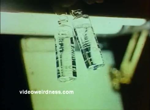 The still from the 'Sandoz Pharmaceuticals/Colors and Chemicals Commercial' features two glass vials being held, possibly showcasing chemical products or pharmaceutical solutions. The vials are transparent, indicating clarity and purity, and the background suggests a laboratory setting. The image conveys a sense of scientific exploration and professionalism, aligned with the educational purpose of the Science Screen Report. The overall tone is informative, aiming to highlight the significance of Sandoz in the fields of pharmaceuticals and chemistry.