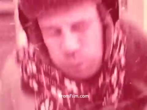 The still from 'Bayer Works Wonders' features a close-up of a man with a focused and intense expression. He appears to be bundled up in winter clothing, including a scarf and possibly earmuffs. The overall tone of the image has a reddish hue, typical of early 1970s film stock. The scene likely captures a moment of determination or effort connected to the theme of Bayer's messaging in the era.