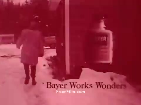 The still from 'Bayer Works Wonders' features a figure walking away from a building in a snowy environment. The scene is tinted in a reddish hue, giving it a vintage aesthetic. Prominently displayed is a bottle labeled 'Bayer,' suggesting a focus on the brand's products. The title 'Bayer Works Wonders' appears at the bottom, indicating the film's promotional nature.