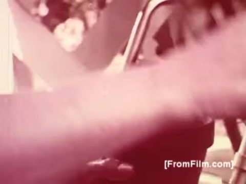 The still from the Muscular Dystrophy PSA features a close-up of an arm reaching towards a car, set against a backdrop that suggests an outdoor setting. The lighting hints at a warm, inviting atmosphere, while the vintage 16mm print gives the image a slightly faded quality typical of mid-20th-century film. Joan Crawford's voice-over emphasizes the message of awareness and support for muscular dystrophy, aligning with the emotional weight of the visuals.