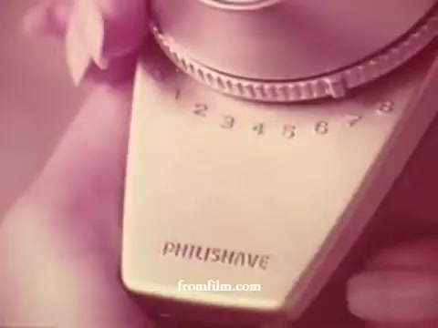 The still features a close-up of a vintage Philishave razor with a dial prominently displaying numbers 1 through 6. The background has a warm, soft focus, likely capturing the cozy, festive mood of a 1970s Christmas advertisement. The overall aesthetic is nostalgic, reflecting the era's design sensibilities.