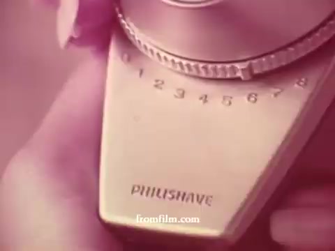 The still features a close-up of a vintage Philishave electric shaver, showcasing its sleek design and dial. The image's soft coloration suggests a warm, nostalgic atmosphere typical of 1970s advertising. The focus is on the shaver's brand and its settings, highlighting the product's functionality in a festive context.