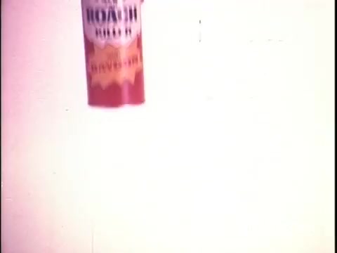 The still features a can of Black Flag bug spray prominently displayed against a light background. The can is labeled 'Roach Killer' with a bold design, suggesting its effectiveness in pest control. The image conveys a vintage aesthetic typical of 16mm film, with a slightly muted color palette and a focus on the product.