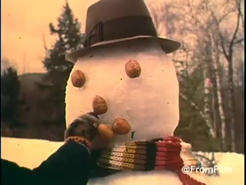 The still from the 'Diamond Nuts Commercial - 1970s' features a snowman adorned with a hat and a colorful scarf. A hand is seen placing Diamond Nuts onto the snowman's body as buttons. The background includes trees, suggesting a winter setting. The overall tone is playful and festive, typical of holiday-themed advertisements from that era.