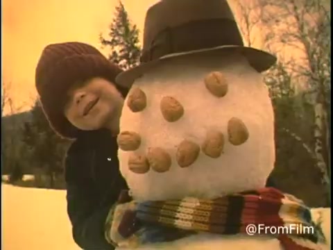 The still features a child in winter attire, playfully embracing a snowman adorned with Diamond Nuts. The snowman wears a hat and has a scarf, adding a cheerful touch to the snowy setting. The scene exudes a warm, nostalgic vibe typical of 1970s commercials.