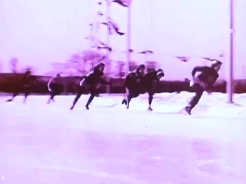 The still features a group of skaters racing on an ice rink, showcasing dynamic movement and athleticism. The scene is likely part of a Mobil I oil commercial, emphasizing performance and speed, with a distinct purple tint giving it a vintage feel. The skaters are in streamlined outfits, capturing the spirit of competition and precision.