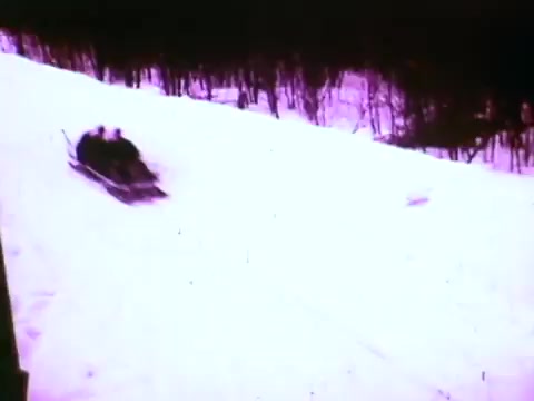 The still from the Mobil I oil commercial features a snow-covered landscape with a snowmobile or sledding activity in motion. The scene captures the excitement of winter sports, emphasizing speed and performance in a snowy environment, likely showcasing the durability and reliability of Mobil I oil in cold conditions. The color tone appears slightly faded, typical of older 16mm film.