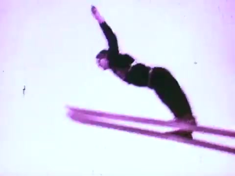 The still features a skier in mid-air, captured during a jump. The skier is positioned horizontally with arms outstretched, showcasing dynamic movement. The background is a stark, light hue, enhancing the action and focus on the skier. This imagery aligns with the theme of performance and precision often highlighted in automotive oil commercials.