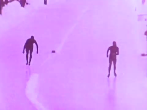The still features two skaters on an ice surface, depicted in a stylized, purple-tinted visual. The focus is on their dynamic movements, highlighting speed and agility, which aligns with the themes of performance and endurance often emphasized in Mobil I oil commercials. The minimalist background suggests an environment designed to showcase the athletes' skills.