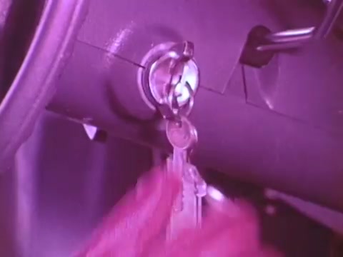 The still depicts a close-up view of a car's ignition system, highlighting a hand inserting a key into the ignition switch. The colors appear to have a pinkish hue, likely due to the film's processing style. This image emphasizes the act of starting a vehicle, tying into the theme of engine performance associated with Mobil I oil.