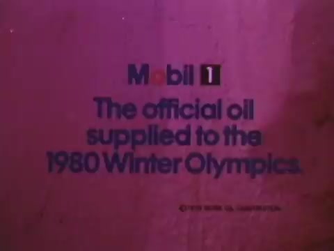 The still features text promoting Mobil I oil, stating that it is the official oil supplied to the 1980 Winter Olympics. The visual background is likely simplistic, focusing on the message. The colors are likely muted, fitting the aesthetic of that era in advertising.
