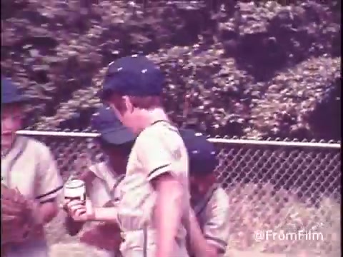 The still from the 1970s Hunt's Snack Pack Chocolate Pudding commercial features a group of kids in vintage baseball uniforms, gathered on a field. They appear to be enjoying the moment, perhaps celebrating with a Snack Pack pudding. The nostalgic vibe is accentuated by the soft color tones typical of 16mm film. The tagline suggests that Snack Pack adds fun to any gathering, highlighting its appealing taste.