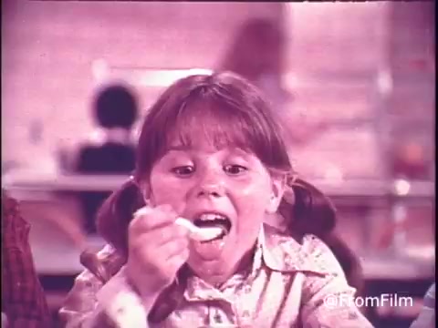 This 16mm still features a young girl joyfully eating Hunt's Snack Pack Chocolate Pudding, highlighting the fun and excitement around the product. The nostalgic atmosphere reflects the 1970s vibe, with vibrant colors and a child-friendly environment. The slogan emphasizes that enjoying Snack Pack makes for a festive experience, aligning with the playful tone of children's advertising from that era. The image captures a moment of pure delight, showcasing the simplicity and enjoyment of pudding in a communal setting.