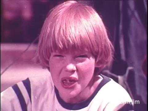 The still captures a moment from a 1970s Hunt's Snack Pack Chocolate Pudding commercial. It features a young boy with bright red hair, expressing excitement or enthusiasm, likely about the pudding. The nostalgic vibe of the image, combined with the tagline about making pudding a party, evokes a sense of carefree childhood associated with that era. The use of 16mm film adds to the vintage aesthetic, reminiscent of a playful and colorful time. Ideal for fans of #StrangerThings seeking retro references.