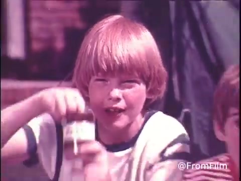 The still from the 1970s Hunt's Snack Pack Chocolate Pudding shows a cheerful young boy with light brown hair, enthusiastically holding up a container of pudding. He appears to be in a casual setting, perhaps outdoors, conveying a sense of fun and enjoyment. The vibrant colors of the 16mm print evoke nostalgia, aligning with the playful tagline about making pudding a party. This visual captures the spirit of childhood and the excitement associated with tasty treats from that era.   Follow us on Twitter @FromFilm.