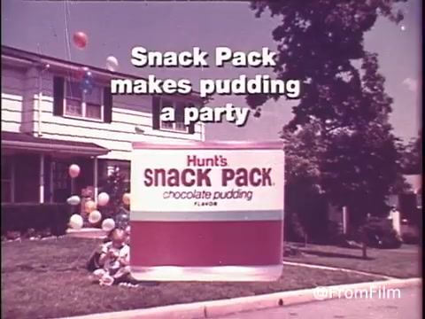 The 16mm still features a vibrant, nostalgic scene promoting Hunt's Snack Pack Chocolate Pudding from the 1970s. In front of a suburban home, a large, colorful package of Snack Pack stands out, emphasizing the tagline 'Snack Pack makes pudding a party.' Balloons float in the background, enhancing the cheerful, festive atmosphere. The retro aesthetic captures the spirit of the era, making it a perfect fit for the playful tone of #strangerthings.