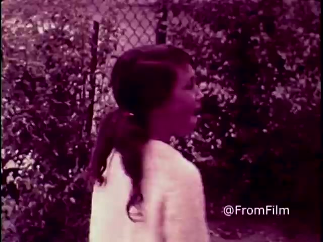 In this still from the 1970 PSA 'Why do you think they call it dope?', a young woman is seen in profile, her expressive face conveying emotion as she engages in conversation. The image is tinged with a reddish-purple hue typical of 16mm prints from that era. Behind her, a chain-link fence and lush greenery create a backdrop that hints at an outdoor setting, possibly emphasizing themes of youth and the environment surrounding the anti-drug message.   Follow us for more insights on film history @FromFilm.