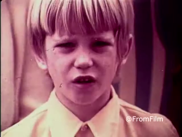 The still from the 1970 PSA 'Why Do You Think They Call It Dope?' features a young boy with blond hair, looking directly into the camera with a serious expression. He appears to be conveying a message about the dangers of drug use. The image's color and graininess reflect the film's vintage quality, typical of a 16mm print from that era. The overall tone emphasizes a serious and cautionary approach to discussing drugs.   For more film insights, follow us on Twitter @FromFilm.