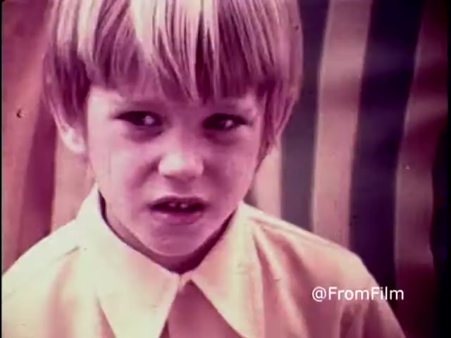 The still features a young boy with a concerned expression, looking directly at the camera. His short, light-colored hair and serious demeanor suggest an earnestness, reflective of the serious themes in the PSA. The background consists of striped patterns that add a vibrant yet contrasting visual element. This 1970 anti-drug public service announcement aims to provoke thought about the consequences of drug use, encapsulated in the provocative question, 'Why do you think they call it dope?'