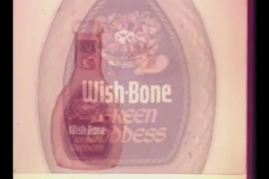 The still features a vintage advertisement for Wish-Bone Green Goddess salad dressing, prominently displaying the bottle in the foreground against a backdrop that includes a decorative plate with salad elements. The design reflects 1960s aesthetics, with bold colors and a playful presentation typical of the era's commercials. The commercial is associated with an ABC Wednesday Night Movie bumper, indicating its broadcast context.