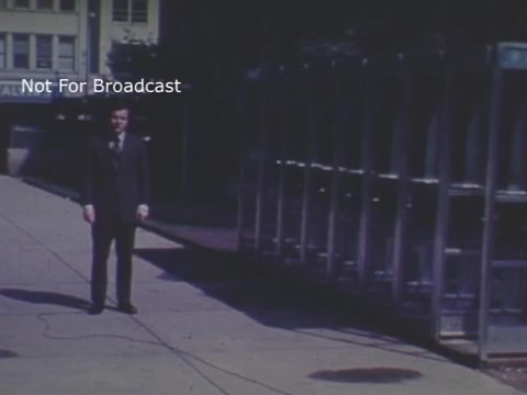 The still features a medium shot of a man in a suit standing on a sidewalk next to a row of telephone booths. The scene is set outdoors, indicating a public area. The image appears to be from a 1970s PSA focused on child abuse, with a muted color palette typical of that era. A 'Not For Broadcast' label suggests it was intended for private use or screening.
