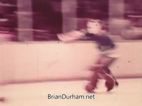 The 16mm still from the '1973 NBC NHL Bumper Promo' features a blurred image of a hockey player in motion, likely skating or preparing to take a shot. The overall color tone appears warm, contributing to a nostalgic feel, typical of the era's broadcast style. The background suggests an ice rink setting, indicative of a hockey game atmosphere.
