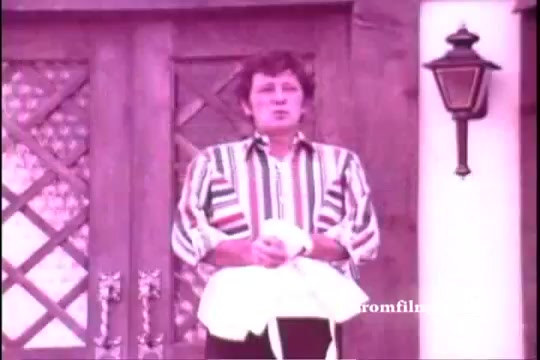 The still from the 1971 'Old Milwaukee Beer' commercial features Bernie Kopell standing in front of a rustic wooden door. He wears a colorful striped shirt and holds a towel, likely participating in a humorous or lighthearted moment. The image has a vintage tone typical of 16mm prints, capturing the essence of classic advertising.