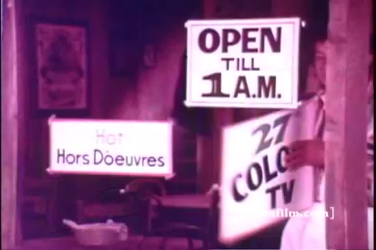 The still features signs promoting an establishment that is 'OPEN TILL 1 A.M.' and advertising 'Hot Hors D'oeuvres' and '27 COLOR TV.' A person, possibly a staff member, is seen holding one of the signs. The overall tone is nostalgic, characteristic of early 1970s advertising, with a focus on hospitality and entertainment. The print has a warm, vintage aesthetic typical of 16mm film.