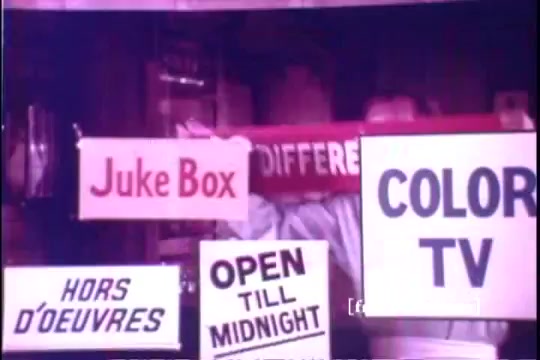 The still features a vibrant scene from the 1971 Old Milwaukee Beer commercial, showcasing various signs that include 'Juke Box,' 'Hors D'oeuvres,' 'Open Till Midnight,' and 'Color TV.' The playful atmosphere hints at a lively, inviting locale. The image captures the nostalgic charm of the era, with bold typography emphasizing different offerings.