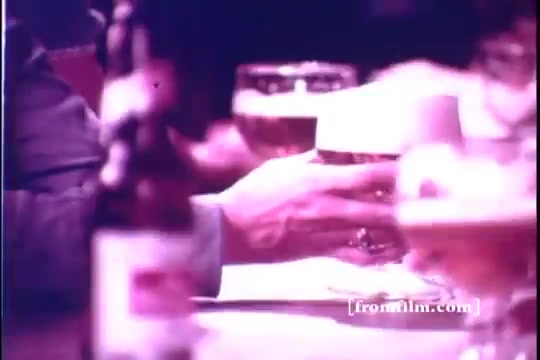 The still from the 'Old Milwaukee Beer' commercial features a close-up of hands reaching for beer glasses on a table. A focus on the frothy mugs suggests a social or celebratory moment. The low quality of the 16mm print adds a nostalgic vibe, typical of advertisements from the 1970s. The overall atmosphere conveys camaraderie and enjoyment associated with sharing a drink.