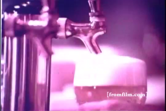 The still from the 1971 'Old Milwaukee Beer' commercial features a close-up of a beer tap dispensing foam into a glass. The lighting is soft and warm, creating a nostalgic atmosphere. The beer has a golden hue and a frothy head, emphasizing its refreshing appeal. The context suggests a focus on enjoyment and quality, typical of beer advertisements from that era.