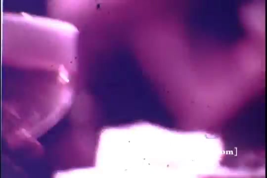 The still from the 1971 Old Milwaukee Beer commercial features a hazy, vintage look typical of 16mm film. It shows a close-up of a glass of beer, possibly being raised or enjoyed. The scene conveys a lively atmosphere, emphasizing social enjoyment. The colors are muted, with a slight purple tint, reflecting the era's film quality.