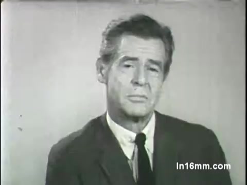 The still shows a somber Robert Ryan, dressed in a suit and tie, addressing the camera with a serious expression. The background is plain, suggesting a focus on his message. This image is part of a public service announcement for Religious Overseas Aid from the 1966 Spring Campaign, highlighting the importance of charitable support.