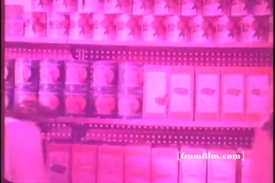 The still from the 'Bonanza Restaurant commercial' depicts a grocery aisle with shelves lined with colorful canned goods and boxes, including items like peaches. The image has a pink hue, indicating it is a print from a 16mm film. The context links it to the Bonanza Steakhouse chain, reflecting the brand's mid-20th century marketing approach.