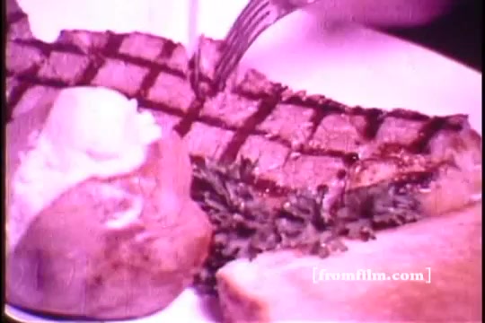 The still from the 'Bonanza Restaurant' commercial features a close-up of a deliciously grilled steak, showcasing distinct grill marks. Accompanying the steak is a baked potato topped with a dollop of butter and a slice of bread on the side. This imagery emphasizes the hearty, inviting nature of the restaurant's offerings, typical of a 1960s steakhouse appeal.