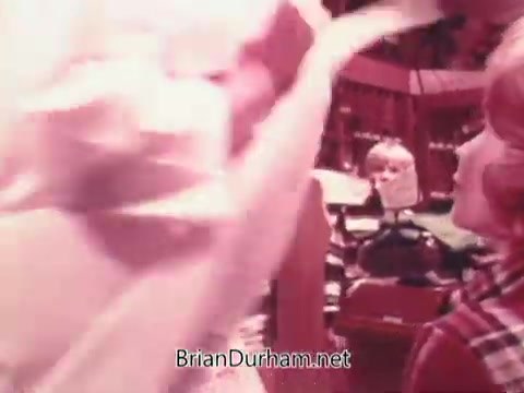 The still from the 'Oxydol detergent commercial' features a scene with several individuals in a domestic setting. A woman is prominently displaying a freshly laundered white garment, suggesting cleanliness and freshness associated with the product. In the background, another person is observing, while the overall atmosphere appears cheerful and lively, typical of 1970s advertising aesthetics. The colors are vibrant, enhancing the nostalgic feel of the era.