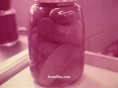 The still features a jar filled with pickles, depicted in a pinkish hue typical of 16mm film. The focus appears to be on the product inside the jar, showcasing the contents prominently. This image may be part of a series highlighting various foods available at Chatham supermarkets, possibly emphasizing freshness and quality. The overall aesthetic aligns with vintage advertising styles, aiming to attract customers.
