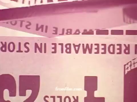 The 16mm still from 'Chatham Supermarket Commercials' features various grocery items and promotions. Key elements include vivid titles such as 'apples,' 'bananas,' 'meats,' and 'steak,' alongside visuals of carts and coupons. The imagery suggests a focus on fresh produce and price comparisons to emphasize value and savings for shoppers. Overall, the scene captures a lively supermarket atmosphere promoting a wide range of products.