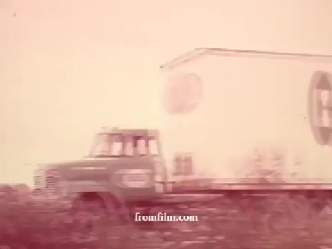 The still from 'Chatham Supermarket Commercials' features a truck driving through an outdoor setting, with a focus on the vehicle's branding. The image captures the essence of grocery supply, hinting at a range of products like apples, bananas, meats, and potatoes. The faded tones give it a vintage feel, typical of 16mm prints, embodying the nostalgic aesthetic of past supermarket advertisements.
